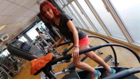 Person trainiert auf einem Climber in einem Fitnessstudio mit weiteren Trainingsgeräten im Hintergrund.