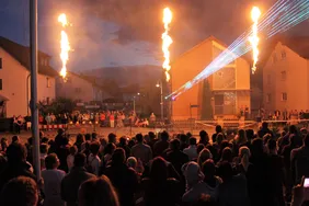 Große Menschenmenge vor einer Bühne mit Flammeneffekten und Lasershow während einer Veranstaltung in der Dämmerung