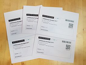 Fünf Teilnahmezertifikate des TYPO3Camp Stuttgart 2017 mit QR-Code liegen fächerförmig auf einem Holztisch und stehen für Weiterbildung und TYPO3-Kompetenz.